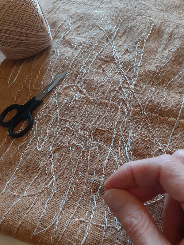 hand embroidering naturally coloured cotton fabric to create a textile artwork